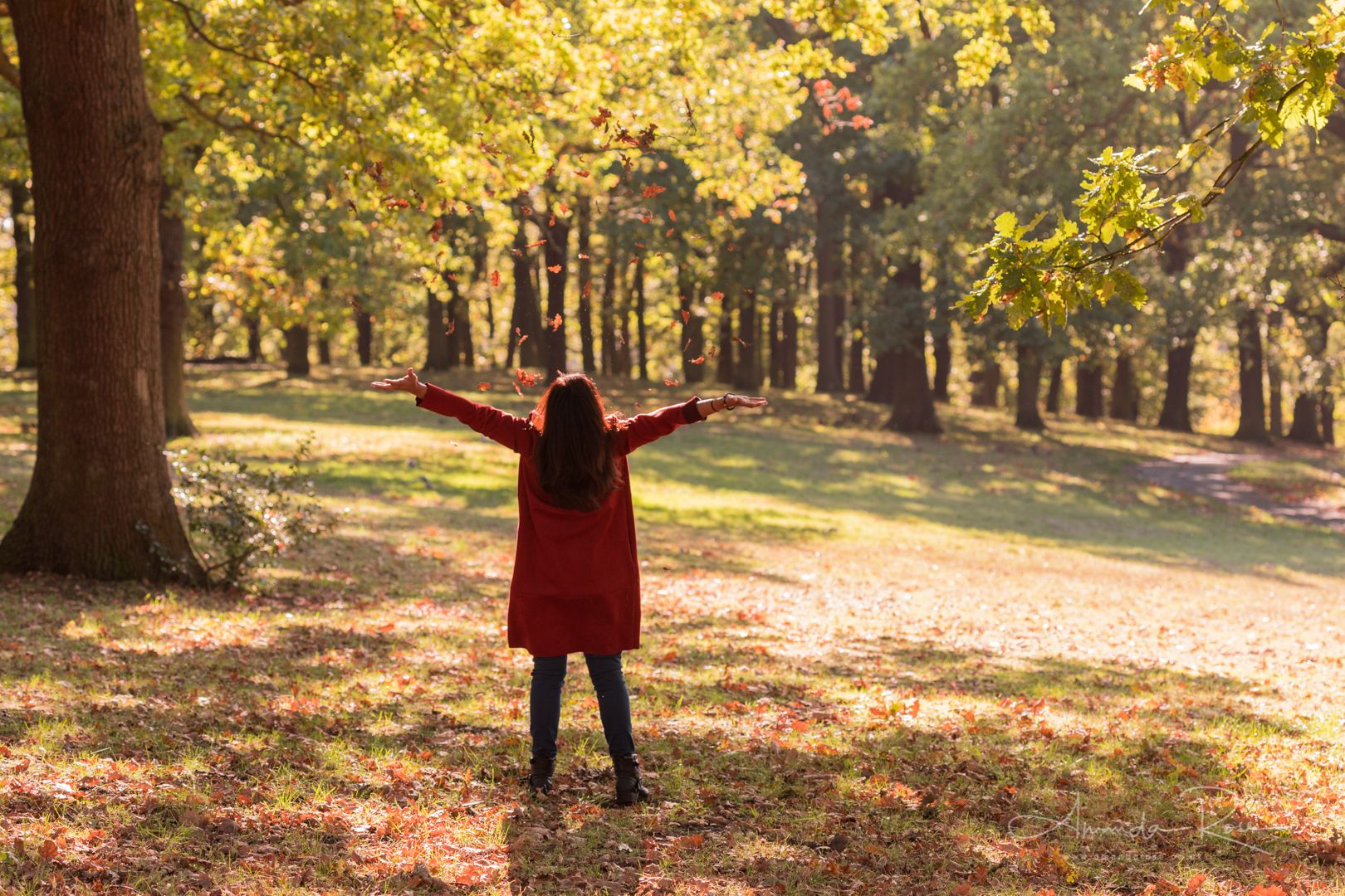 A woman in a red coat standing in an autumn forest, arms open