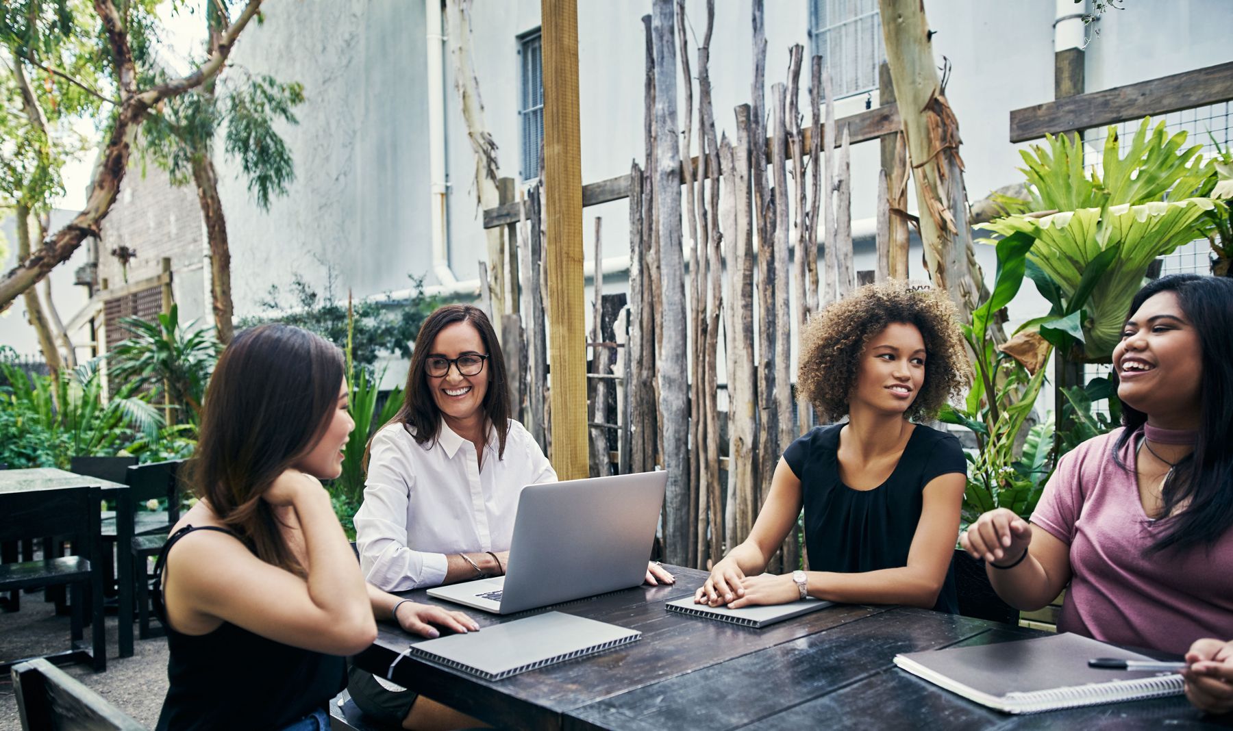 Four women in conversation around a table with a laptop